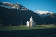 在白雪皑皑的山区背景下，风景如画的白色教堂矗立在晴朗的蓝天下