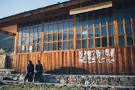 一座质朴的木制建筑，有大玻璃窗，两个人坐在外面的自然光线下