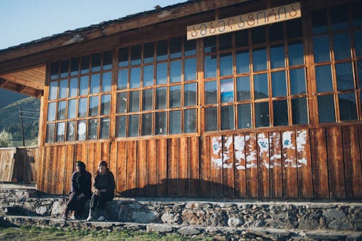 一座质朴的木制建筑，有大玻璃窗，两个人坐在外面的自然光线下