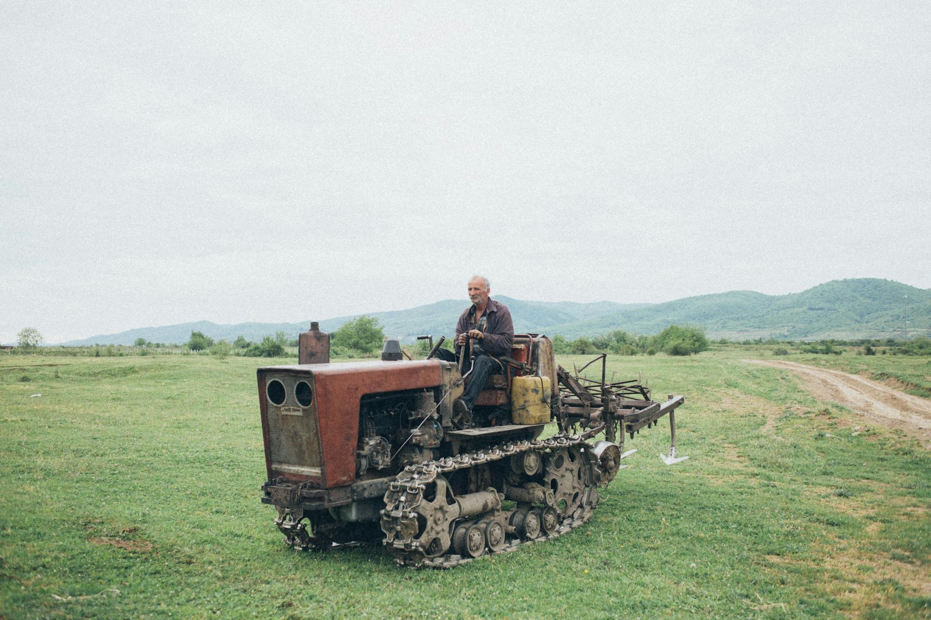 An elderly man driving a vintage tractor across a rural field, showcasing traditional farming.