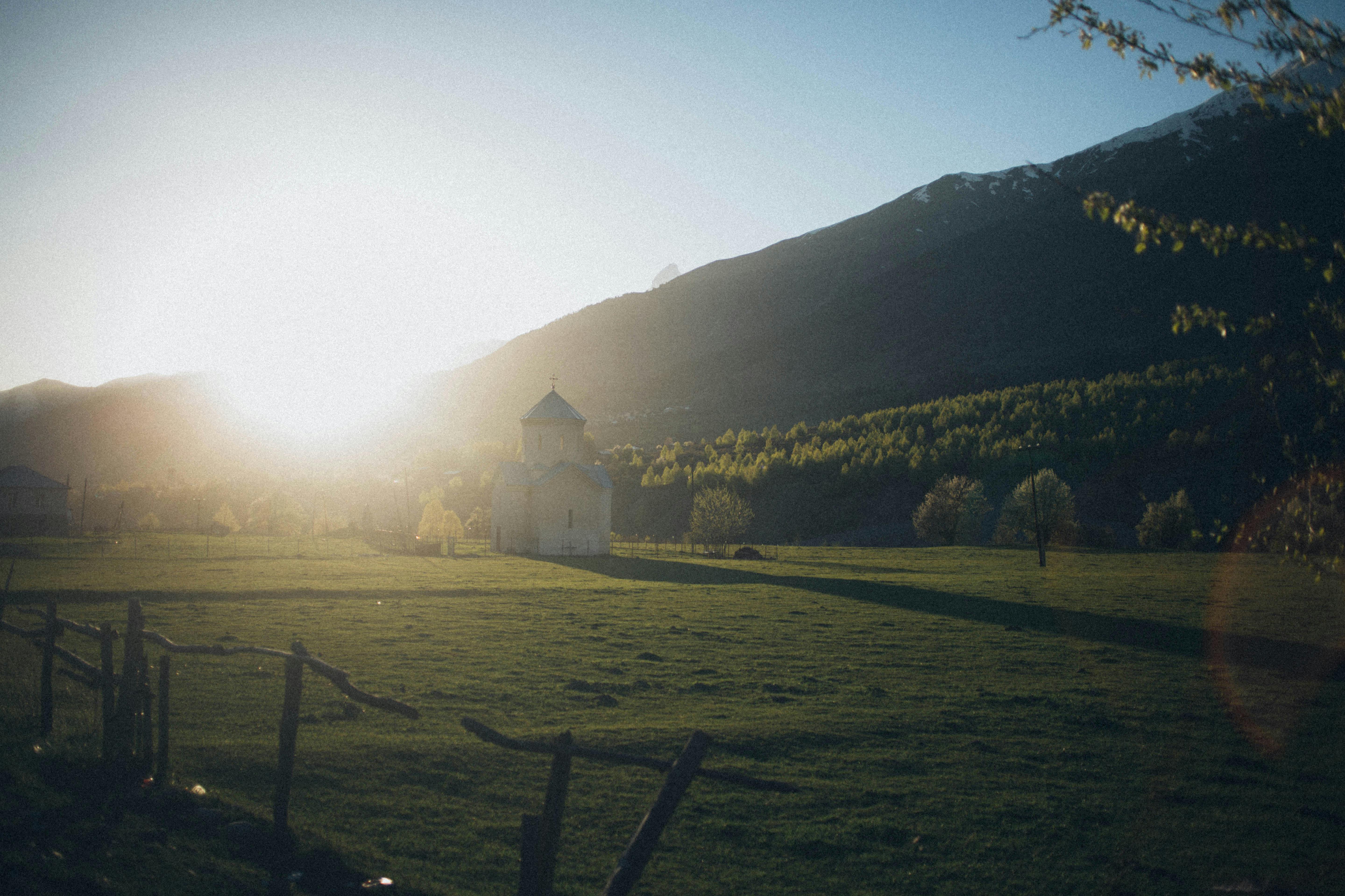 在广阔的田野上，群山环绕着一座孤独的教堂，宁静的日出映照着这一切