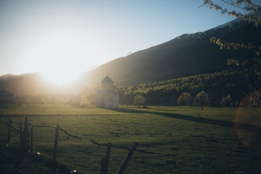 在广阔的田野上，群山环绕着一座孤独的教堂，宁静的日出映照着这一切