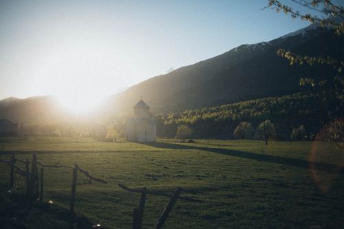Free Serene sunrise over a vast field with a lone chapel, surrounded by mountains. Stock Photo