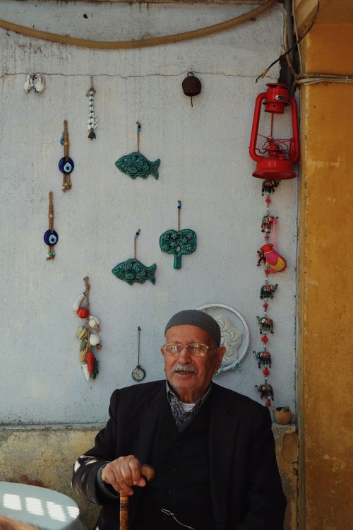 Free Senior man in glasses and hat sitting by a wall adorned with decorative ornaments. Stock Photo