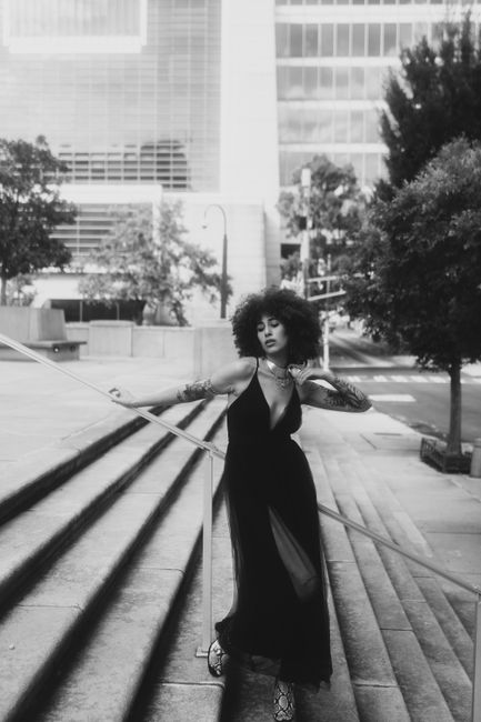 Stylish woman in a black dress posing on city steps, black and white photography.