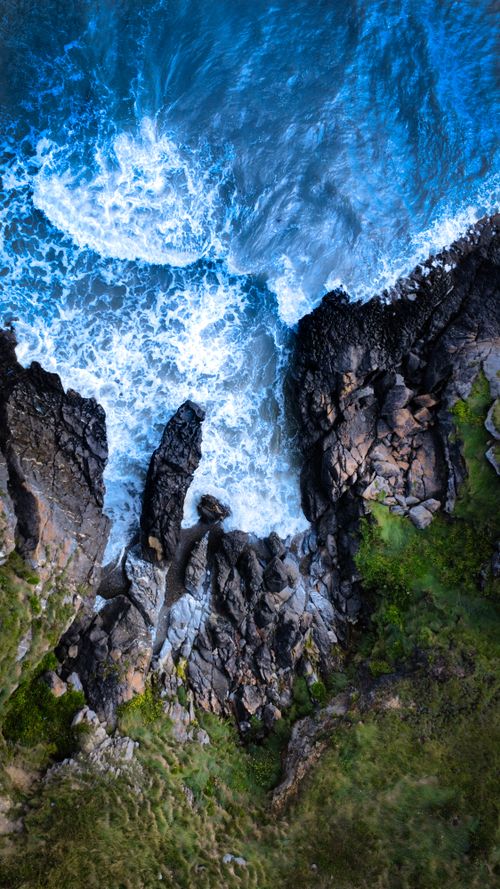 Free A breathtaking aerial view of waves crashing against rugged cliffs and rocks, showcasing nature's raw power. Stock Photo