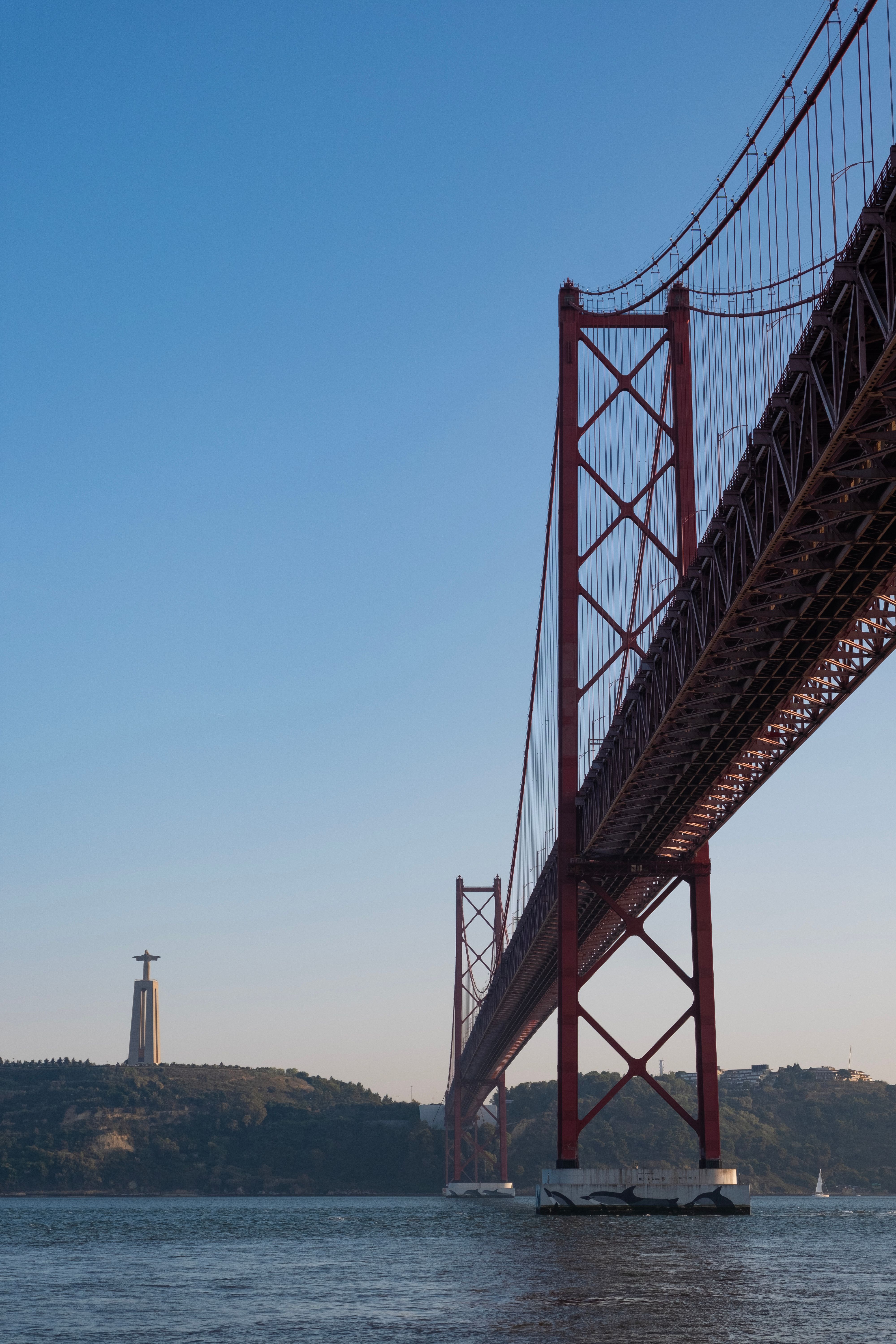 View of the iconic 25 de Abril Bridge and Cristo Rei statue in Lisbon under clear skies.