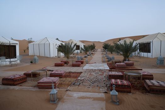 A serene outdoor setup in a desert camp featuring traditional tents, cushions, and lanterns.