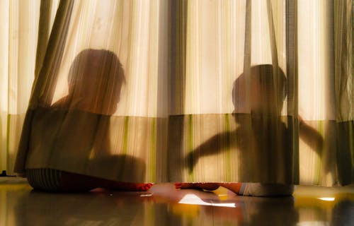 Silhouettes of Two Little Boys Sitting on the Floor behind a Curtain