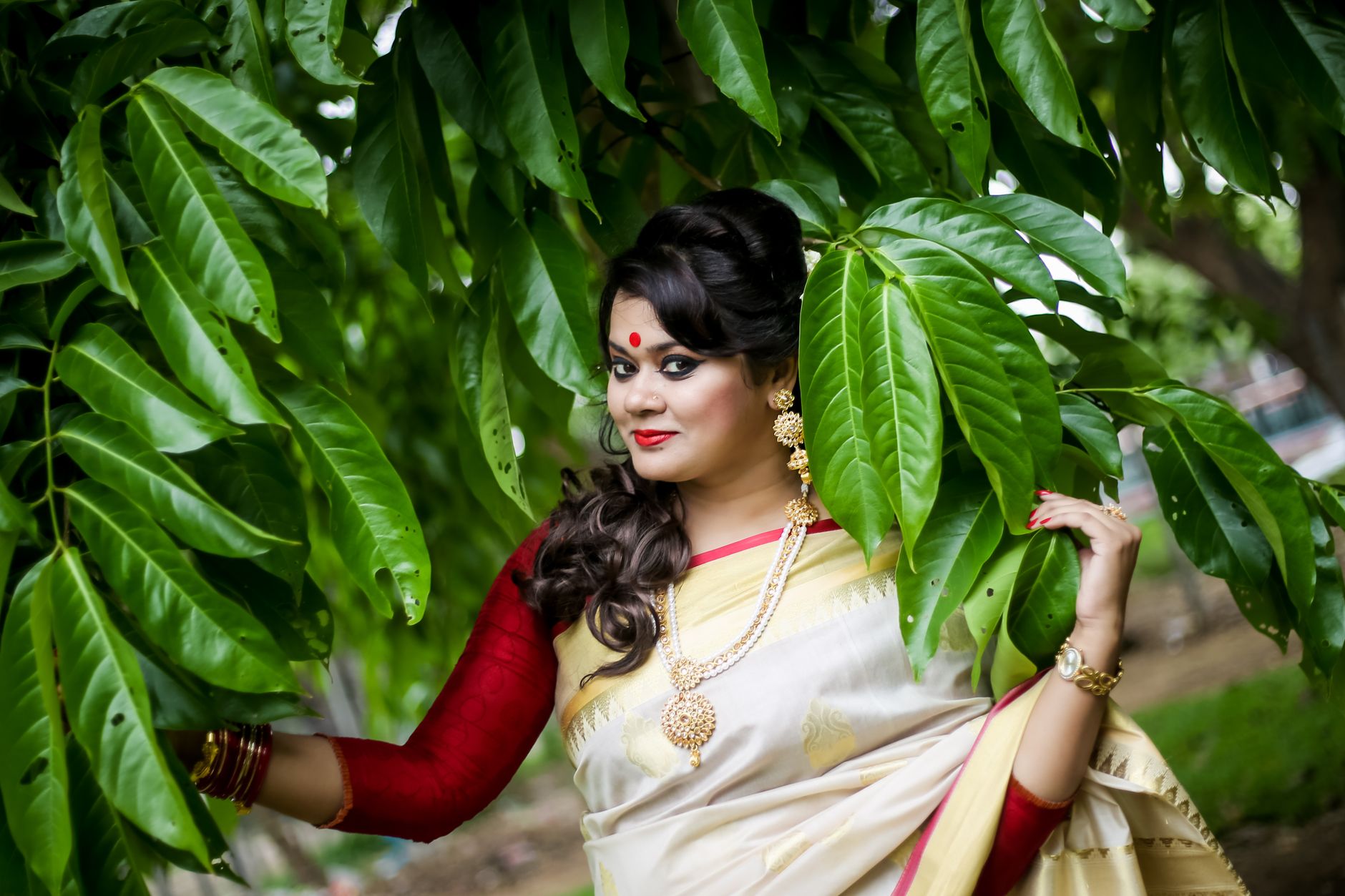 Indian woman in a traditional sari posing outdoors among lush green leaves.