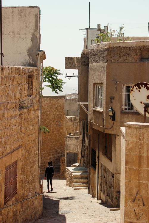 Free A narrow stone street in a historic Mediterranean town with rustic buildings and a lone walker. Stock Photo