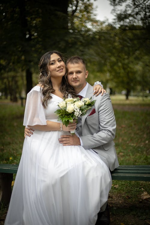 Newlyweds Smiling and Hugging on Bench in Park