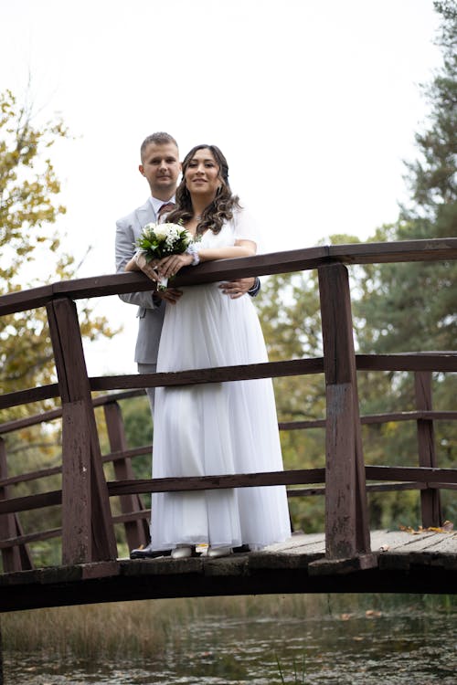 Newlyweds Standing and Embracing on Footbridge