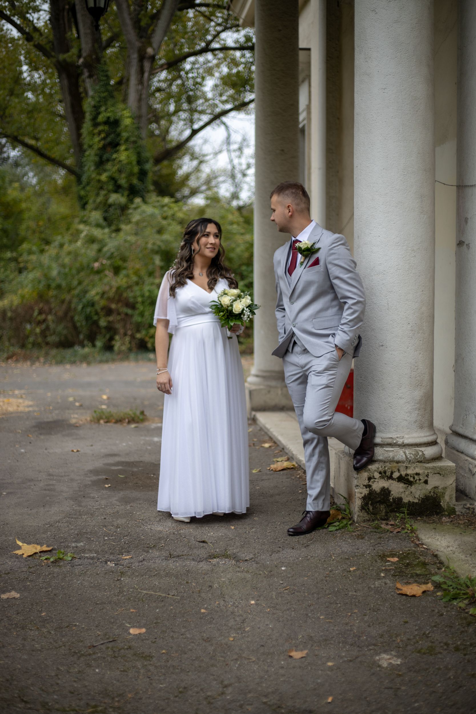 A newlywed couple poses outdoors near classical columns, capturing a romantic wedding moment.