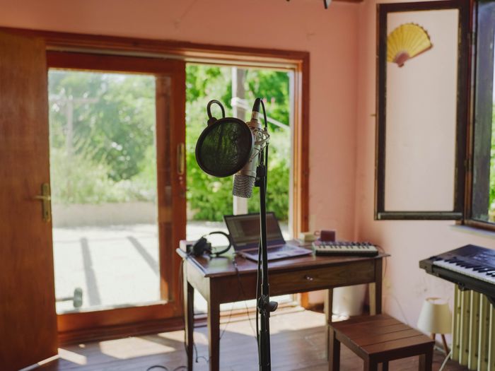 A microphone and laptop on a desk beside a glass door