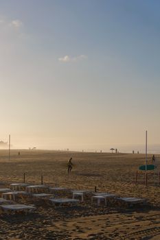 Peaceful Carcavelos beach at sunrise with silhouettes of people and loungers on the sand.