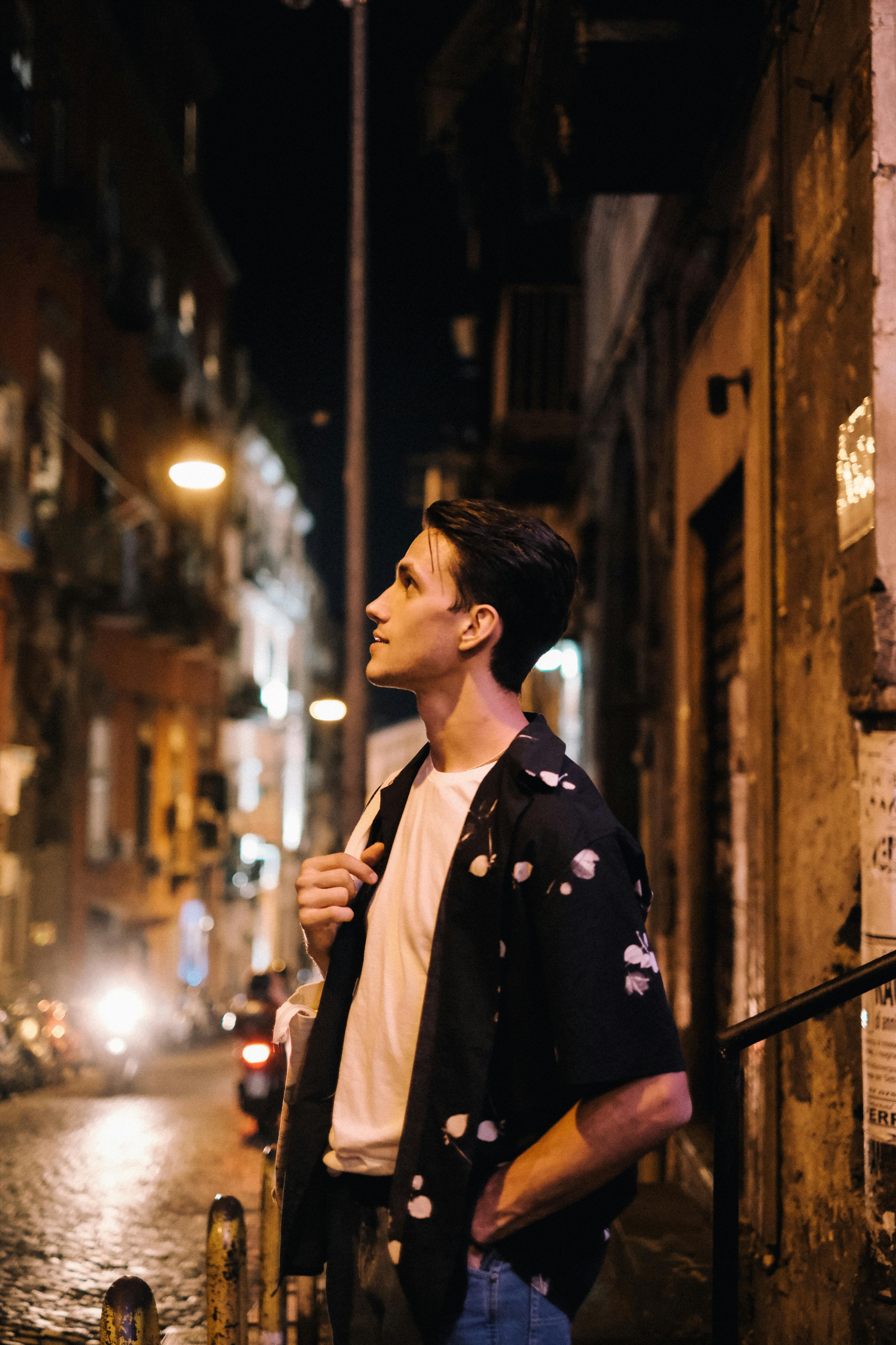 A young man in a white t-shirt and black shirt explores a lively city street at night.