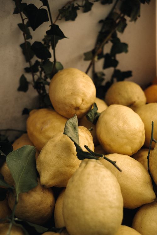 Free A rustic stack of fresh lemons with green leaves and vines in an earthy setting. Stock Photo
