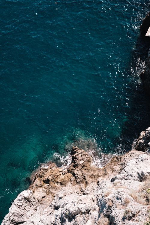 Free Top view of a rugged rocky shoreline and vibrant turquoise sea, showcasing natural erosion. Stock Photo