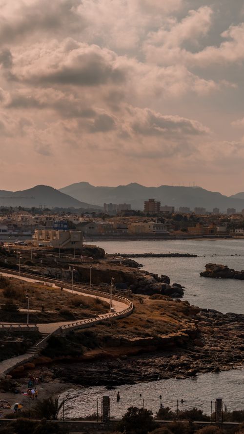 Free A scenic view of Murcia's coastline with urban skyline and mountains at dusk. Stock Photo