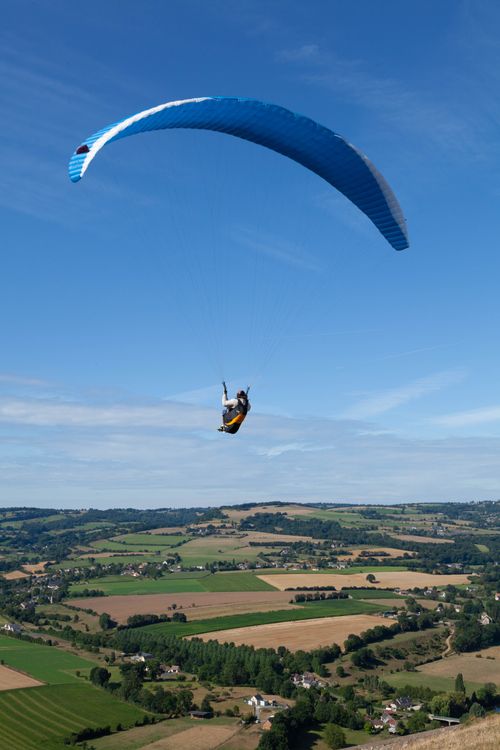 Free Dynamic shot of a paraglider soaring over Clécy's rural landscape in Normandy, France. Stock Photo