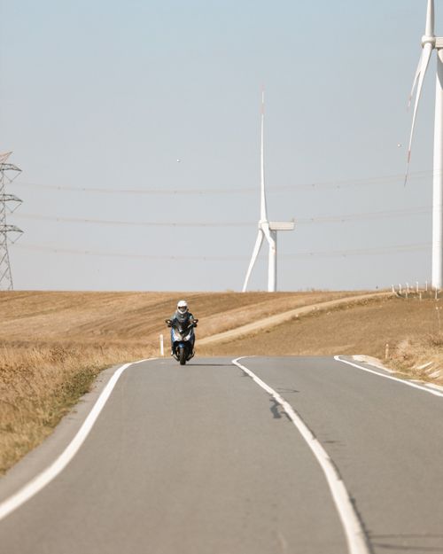 Free A motorcyclist rides on a rural road surrounded by wind turbines under a clear sky. Stock Photo