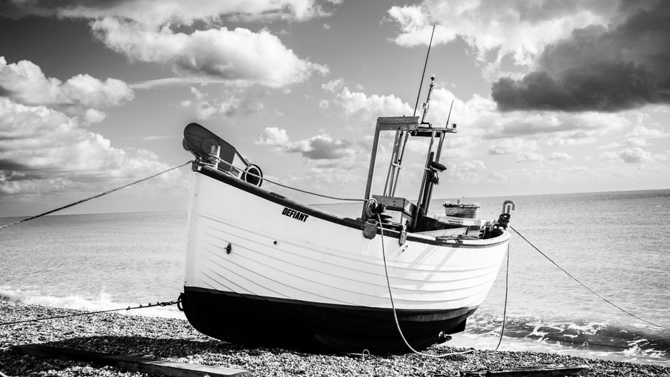 Moored fishing boat on a pebbly beach in a striking black and white setting, with cloudy skies overhead.