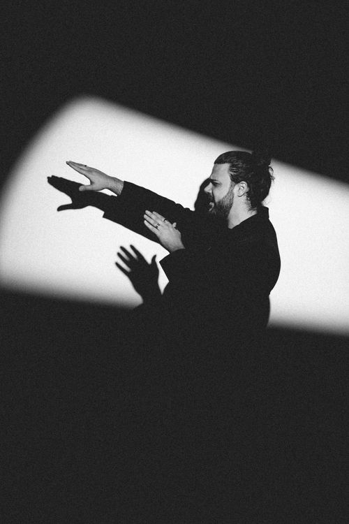 Free Artistic black and white portrait of a man with raised arms casting a shadow. Stock Photo
