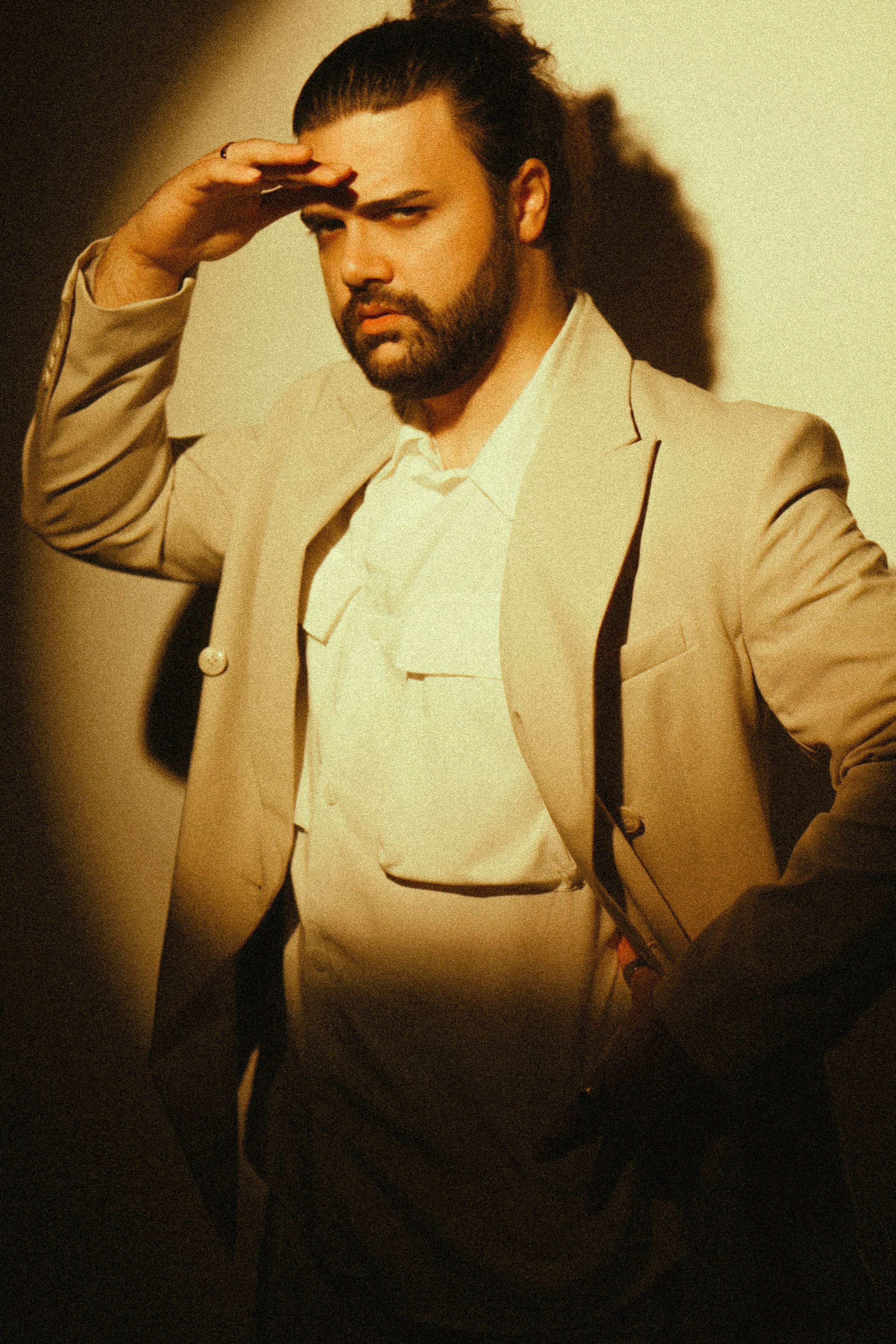 Portrait of a fashionable man in a beige suit saluting, casting dramatic shadows.