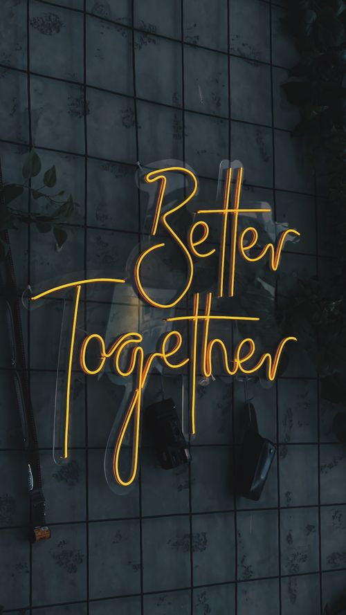 Free Yellow neon sign 'Better Together' on a dark tiled background, highlighting unity and connection. Stock Photo