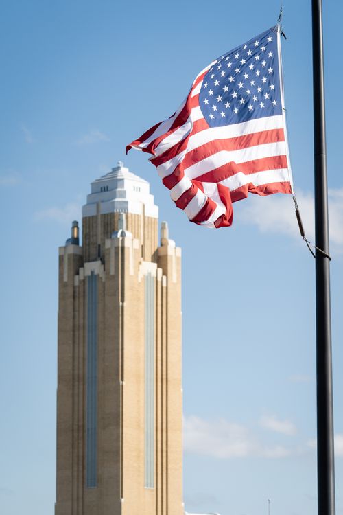 Free Vertical shot of an American flag waving beside a historic tower in Fort Worth, Texas. Stock Photo