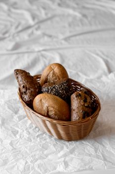 A variety of rustic multi-grain breads displayed in a wicker basket on a crumpled paper background.