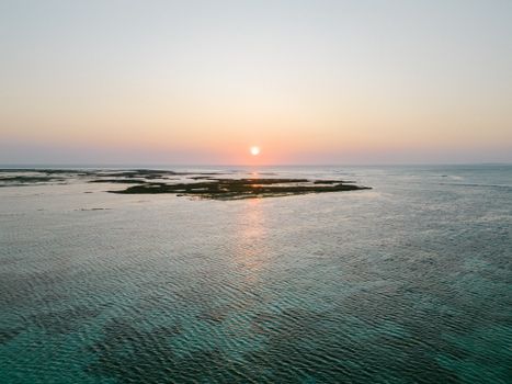 A tranquil aerial shot capturing a breathtaking sunset over the open sea with scattered landmasses.