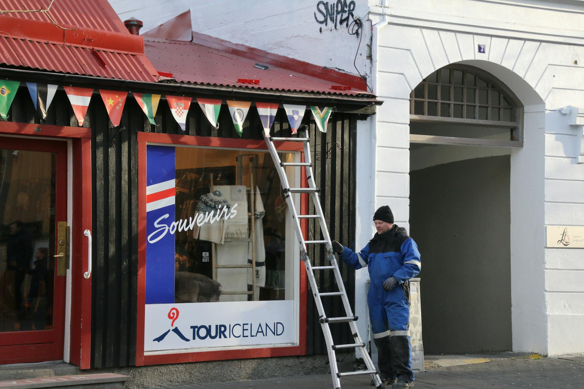 A worker standing outside a Reykjavik souvenir shop with international flags and a ladder.