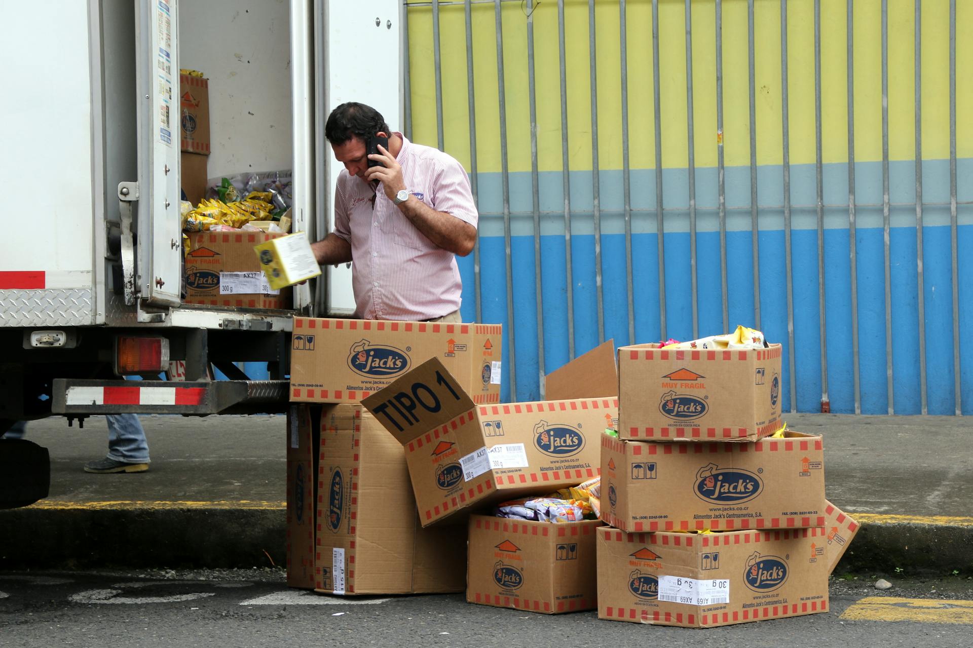 Man unloads cardboard boxes from truck while talking on phone in San José, Costa Rica.