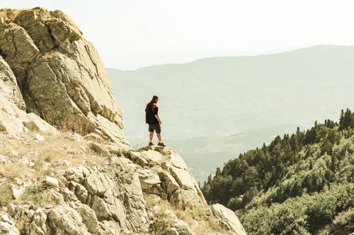 Free A lone hiker stands on a rocky cliff overlooking lush mountains in Bursa, Türkiye. Stock Photo