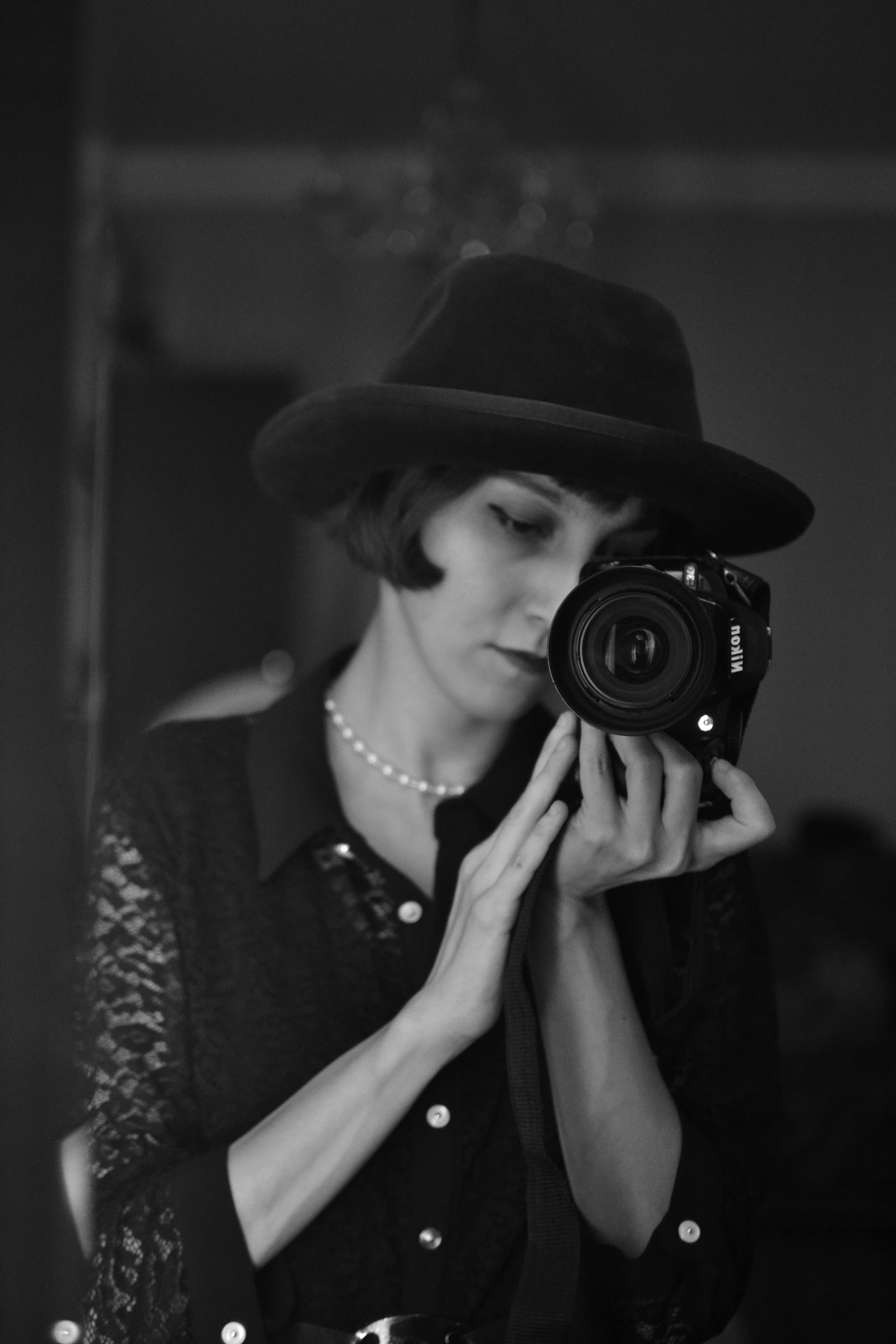 Stylish monochrome portrait of a woman holding a camera, wearing a hat and pearl necklace.