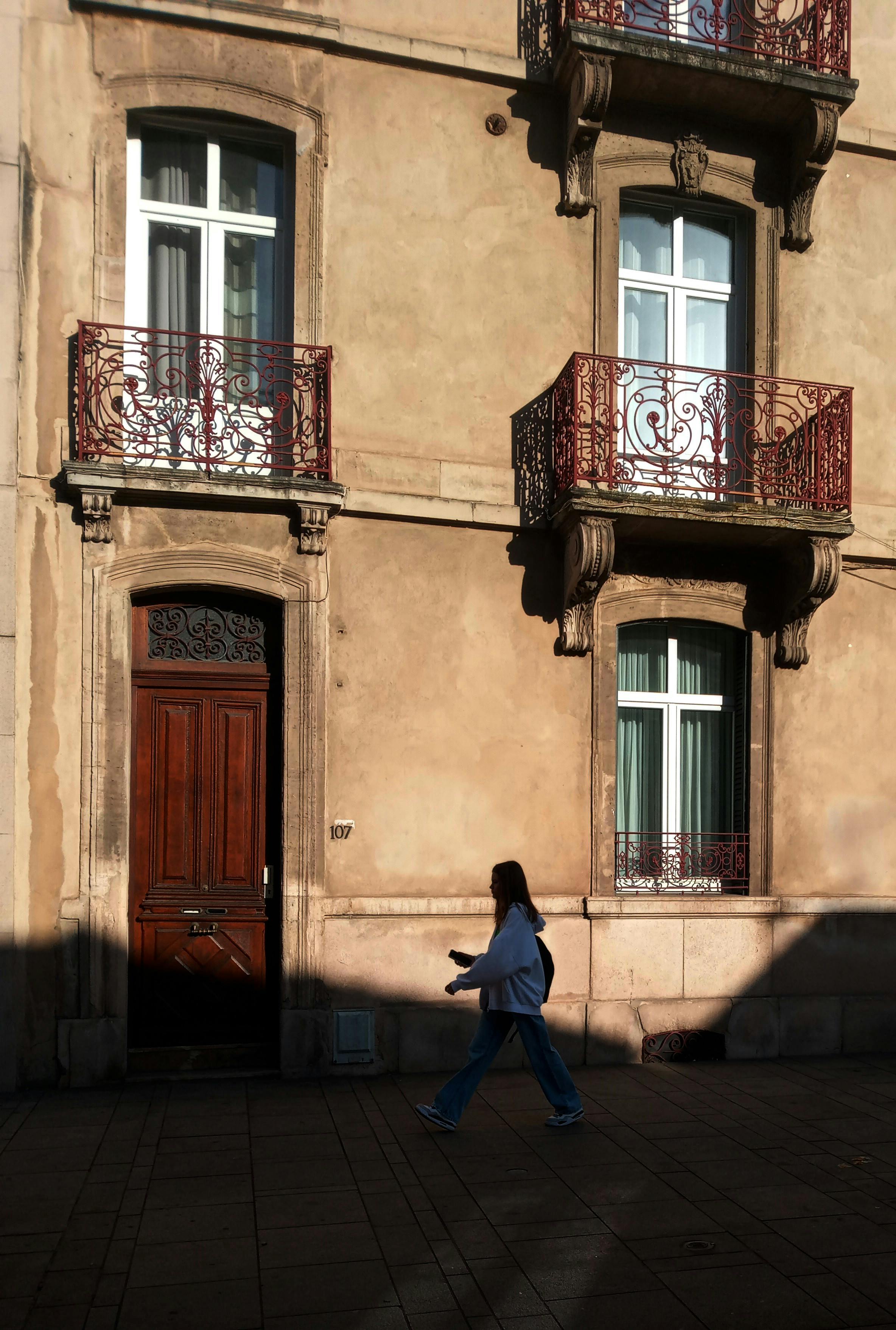 A person walks past a classic residential building in Nancy, France, with ornate balconies.