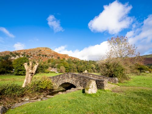 Free Charming stone bridge over a stream in a picturesque rural landscape with mountains and blue sky. Stock Photo