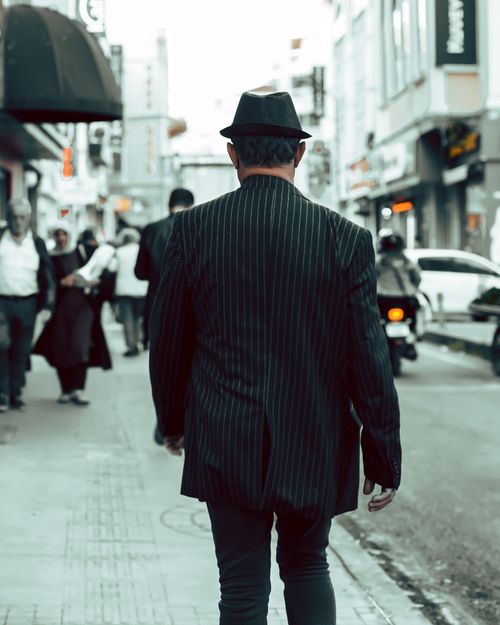 Free A man in a fedora and striped blazer walking down a bustling city street. Stock Photo