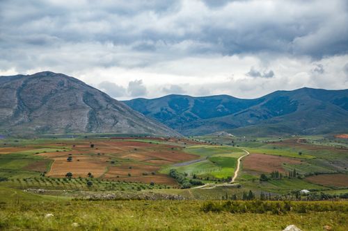 Free Stunning mountain panorama showcasing green and brown farmland under cloudy skies, with a winding path. Stock Photo