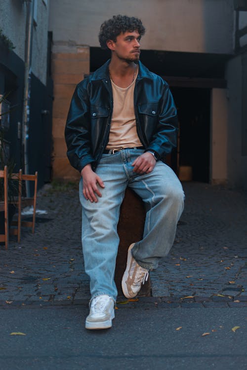 Man in Leather Jacket Sitting on Post by Street