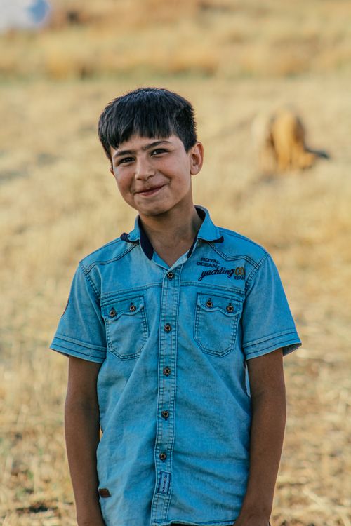 Free Portrait of a boy in a denim shirt smiling outdoors in a rural setting. Stock Photo