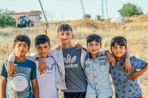 Free Five boys with arms around each other in a rural outdoor setting, smiling and posing for the camera. Stock Photo