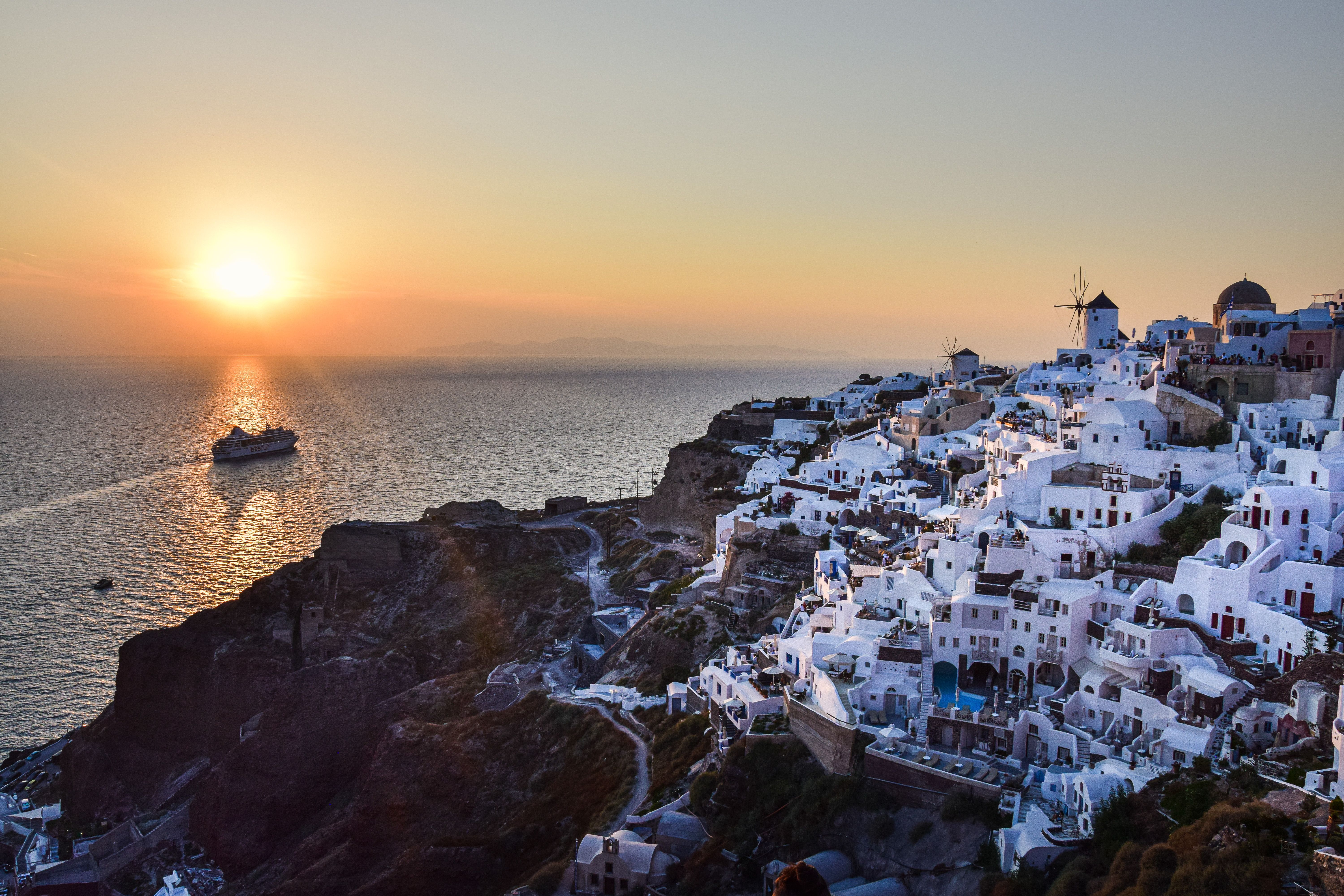 Beautiful sunset view of Santorini's whitewashed buildings and a cruise ship in the Aegean Sea.