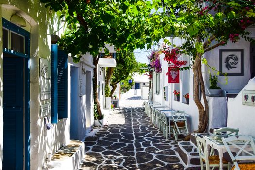 Explore a picturesque Greek street with quaint whitewashed buildings, vibrant flowers, and inviting outdoor seating.