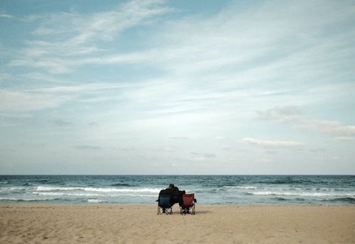 Free A serene moment of a couple sitting on chairs by the seaside under a vast sky. Stock Photo