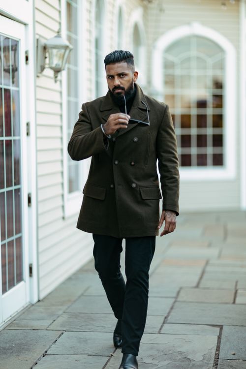 Free Stylish man in green coat walking outdoors, holding sunglasses, exuding confidence. Stock Photo