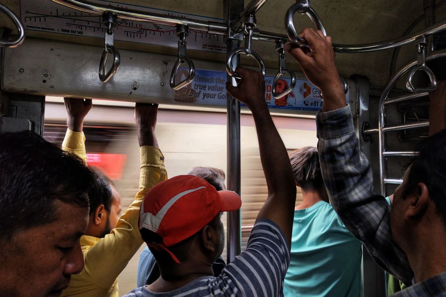 Passengers standing and holding handles inside a busy Mumbai local train.