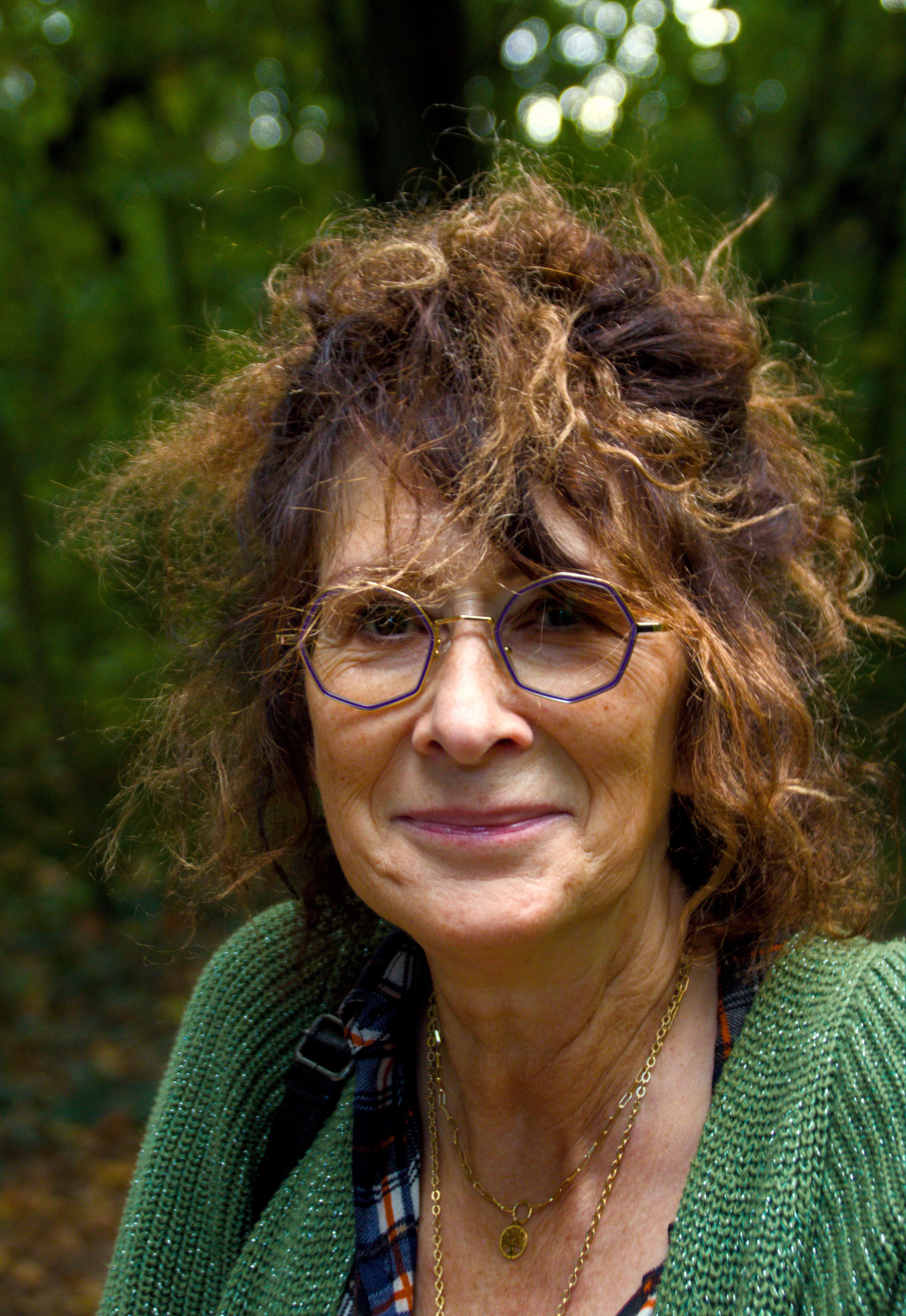 Portrait of a senior woman with eyeglasses and tousled hair in a green forest.